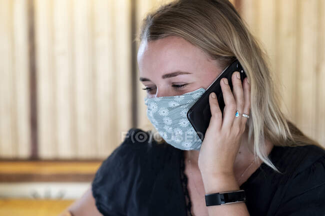 Retrato de jovem loira usando máscara facial azul, usando telefone celular. — Fotografia de Stock
