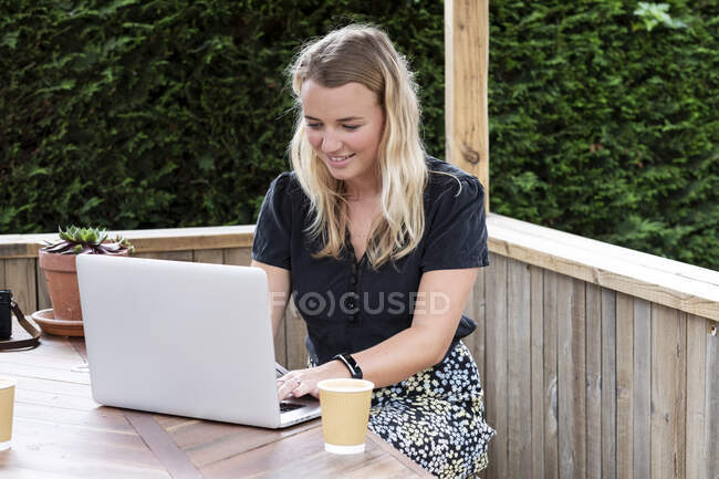 Junge blonde Frau sitzt am Tisch und benutzt Laptop-Computer. — Stockfoto