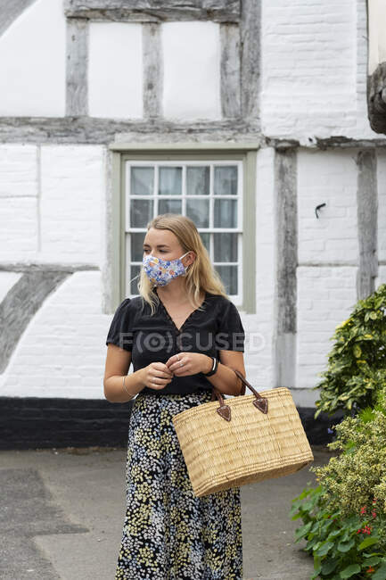 Молода блондинка в масці для обличчя, що йде через село, несе торгову сумку . — стокове фото