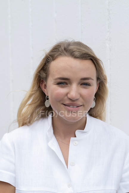 Portrait of young blond woman wearing white blouse, smiling at camera. — Stock Photo