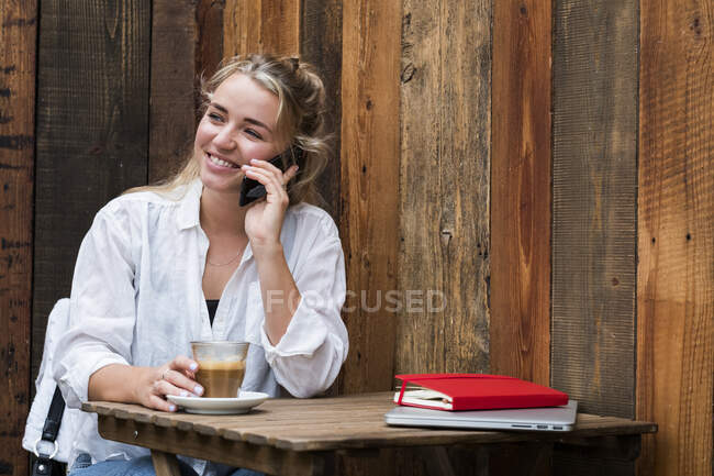 Giovane donna bionda seduta da sola in un caffè, utilizzando il telefono cellulare, lavorando a distanza. — Foto stock