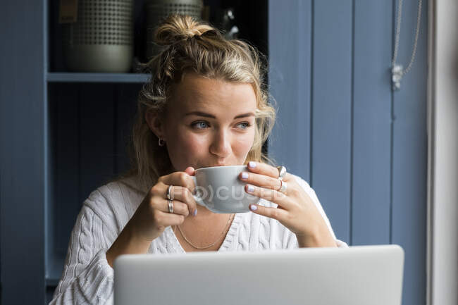 Junge blonde Frau sitzt allein an einem Cafétisch mit einem Laptop und arbeitet aus der Ferne. — Stockfoto