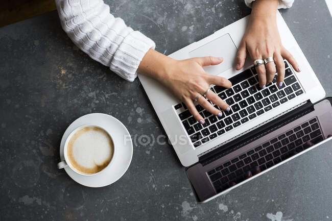 High angle view of woman sitting alone at a cafe table with a laptop, working remotely. — Stock Photo