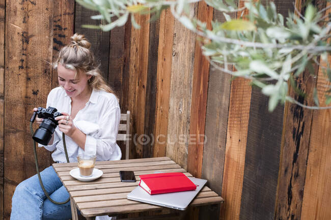 Молода блондинка на відкритому столі дивиться на дисплей цифрової камери.. — стокове фото