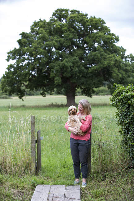 Portrait of smiling woman holding fawn coated young Cavapoo. — Stock Photo