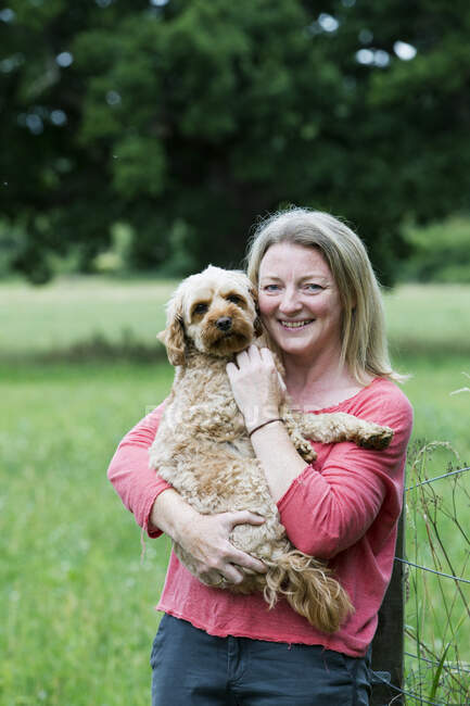 Portrait of smiling woman holding fawn coated young Cavapoo. — Stock Photo