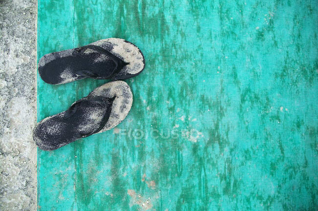 High angle close up of sandy black flip flops on turquoise floor mat. — Stock Photo