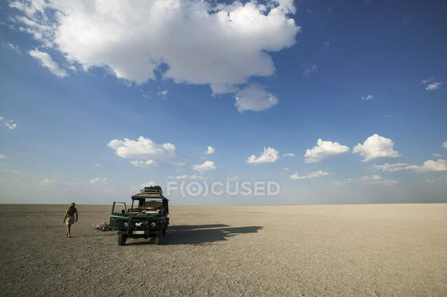 Man walking past 4x4 parked on the Makadikadi Salt Pans in Botswana. — Stock Photo