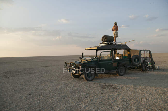 Mann steht auf Fahrzeug, das auf den Makadikadi-Salinen in Botswana geparkt ist. — Stockfoto
