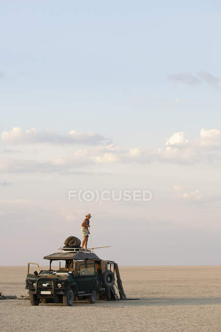 Homem em pé em cima do veículo estacionado nas Panelas de Sal Makadikadi no Botsuana. — Fotografia de Stock
