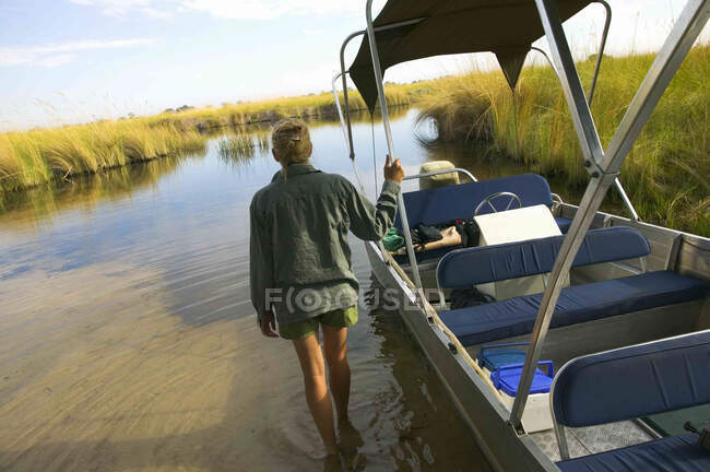 Vista trasera de la mujer vadeando en el agua, empujando barco, Delta del Okavango, Botswana. - foto de stock