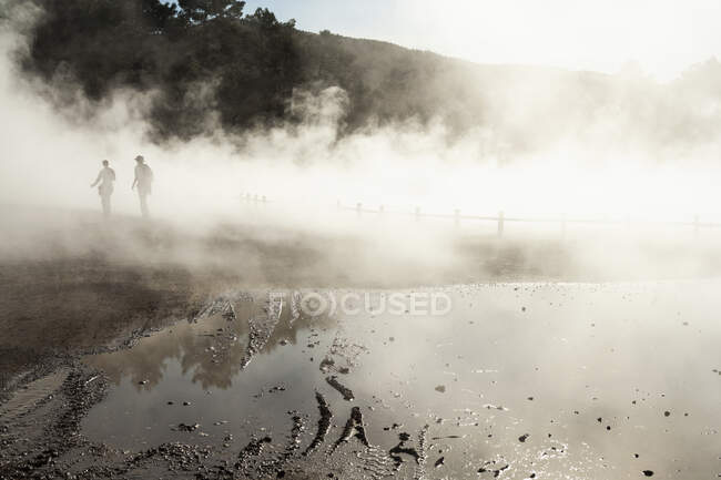 Два человека в тумане, поднимающиеся из термальных бассейнов — стоковое фото