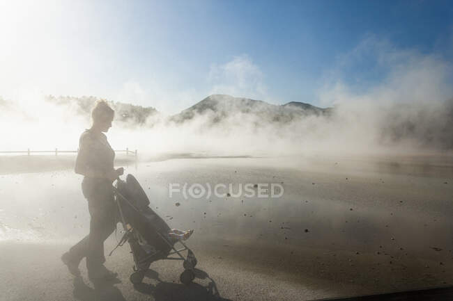 Woman and child in buggy in rising steam from thermal pools — Stock Photo