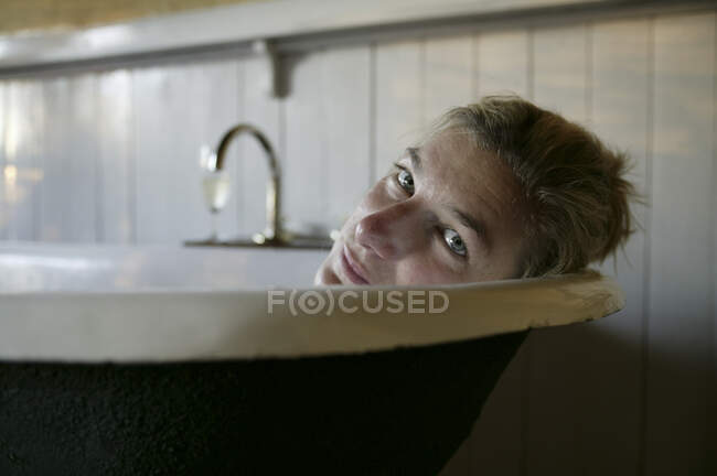 Kopf- und Schulterporträt einer Frau, die in der Badewanne liegt und in die Kamera blickt. — Stockfoto