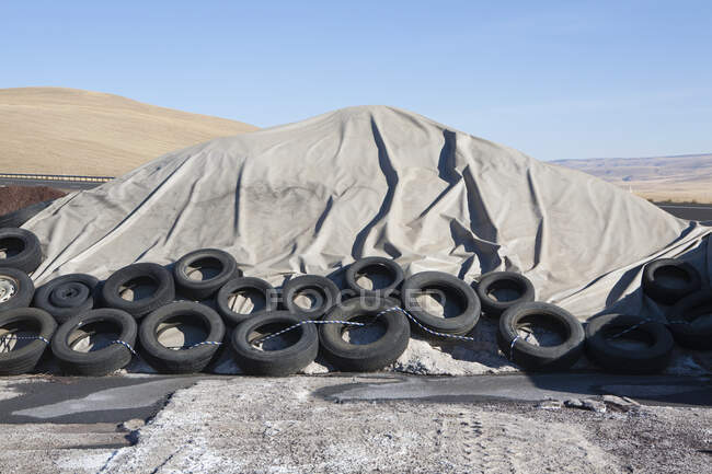 Heap of waste covered with tarpaulin, weighted down by rubber tires. — Stock Photo