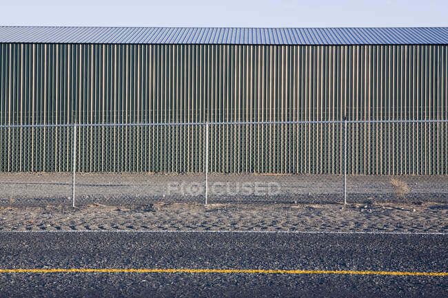 Bâtiment en fer ondulé avec une clôture, par la route — Photo de stock