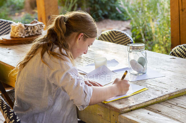 Adolescente escribiendo fuera en la terraza al atardecer. - foto de stock