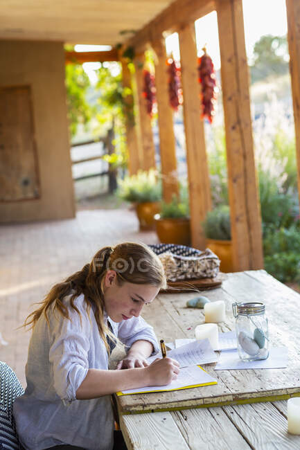 Adolescente escribiendo fuera en la terraza al atardecer. - foto de stock