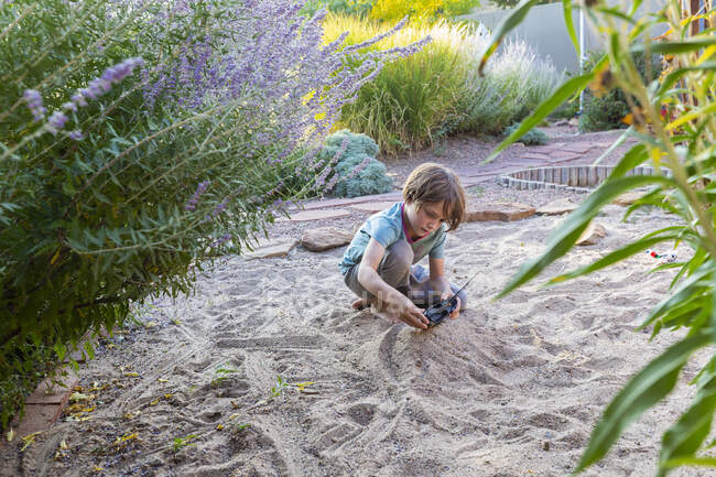 Menino de sete anos jogando no jardim arenoso com seu navio de brinquedo. — Fotografia de Stock