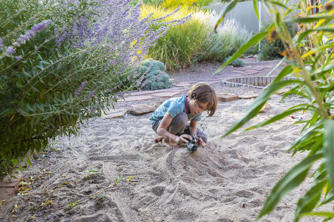 Niño de siete años jugando en el jardín de arena con su barco de juguete. - foto de stock