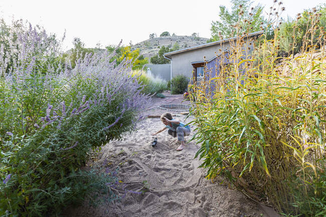 Garçon de sept ans jouant dans un jardin sablonneux avec son bateau jouet. — Photo de stock