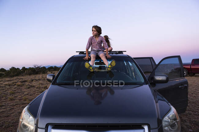 Дівчина-підліток та її молодший брат сидять на позашляховику на заході сонця . — стокове фото