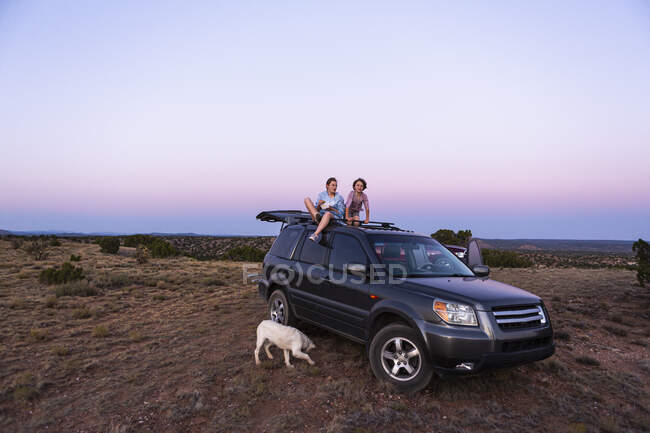 Teenagermädchen und ihr jüngerer Bruder sitzen bei Sonnenuntergang auf SUV-Auto. — Stockfoto