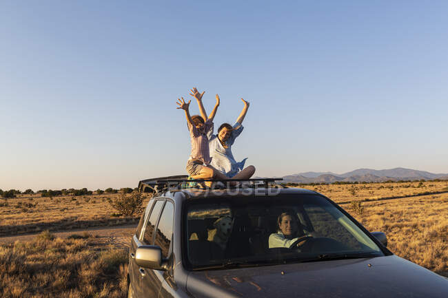 Adolescente menina e seu irmão mais novo no topo do carro SUV dirigindo na estrada do deserto — Fotografia de Stock