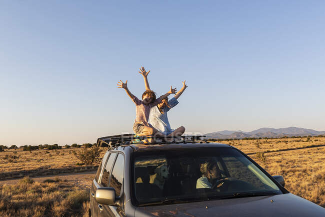 Adolescente chica y su hermano menor en la parte superior de SUV coche de conducción en el camino del desierto - foto de stock