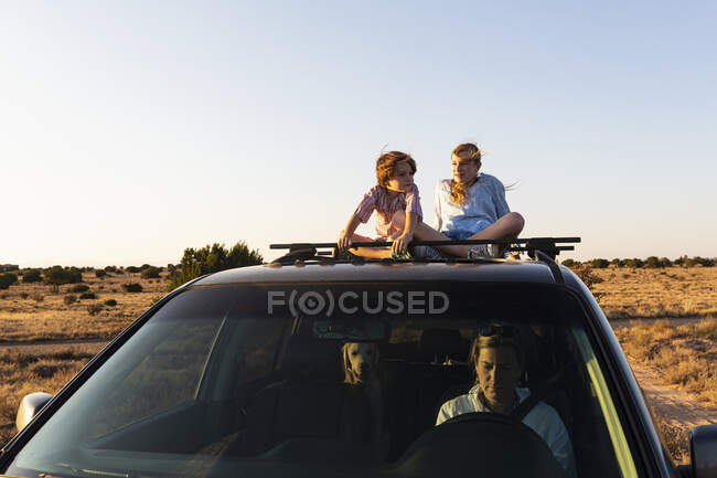 Adolescente et son jeune frère sur le dessus de la voiture SUV conduite sur la route du désert — Photo de stock