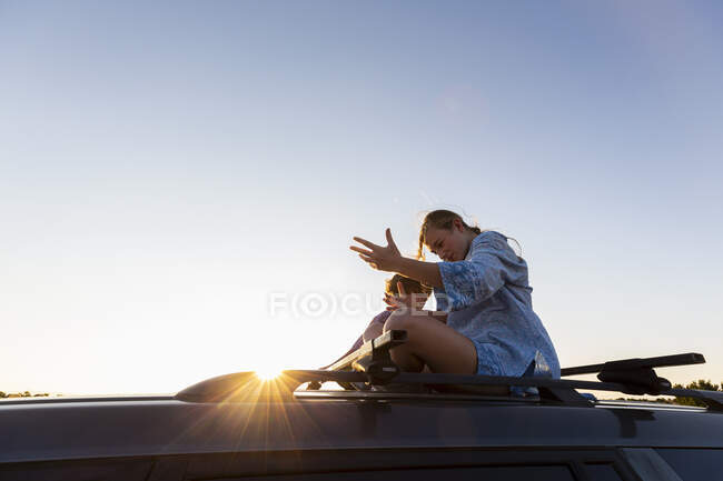 Teenage girl and her younger brother on top of SUV car on desert road, Galisteo Basin, Santa Fe, NM. — Stock Photo