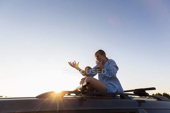 Adolescente e seu irmão mais novo no topo do carro SUV na estrada do deserto, Galisteo Basin, Santa Fe, NM. — Fotografia de Stock