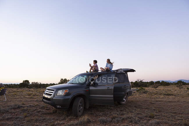 Teenager-Mädchen und ihr jüngerer Bruder sitzen bei Sonnenuntergang auf ihrem SUV. — Stockfoto