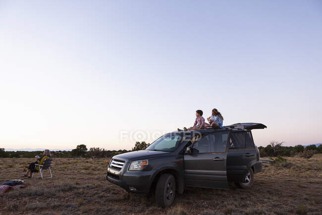 Ragazza adolescente e suo fratello minore seduti in cima al loro SUV al tramonto. — Foto stock