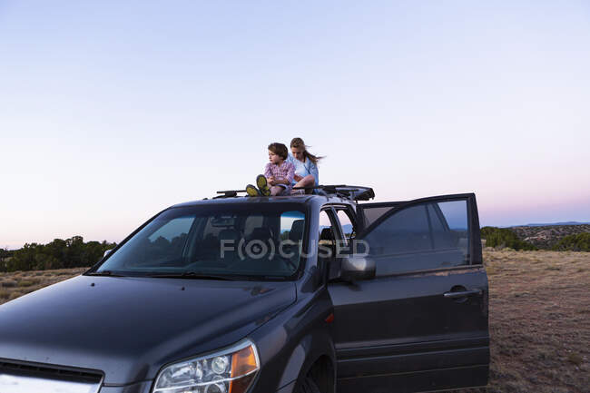 Девочка-подросток и ее младший брат сидят на вершине внедорожника на закате. — стоковое фото