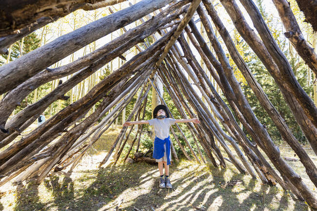 Niño mirando hacia arriba, de pie en un túnel hecho de troncos de árboles. - foto de stock
