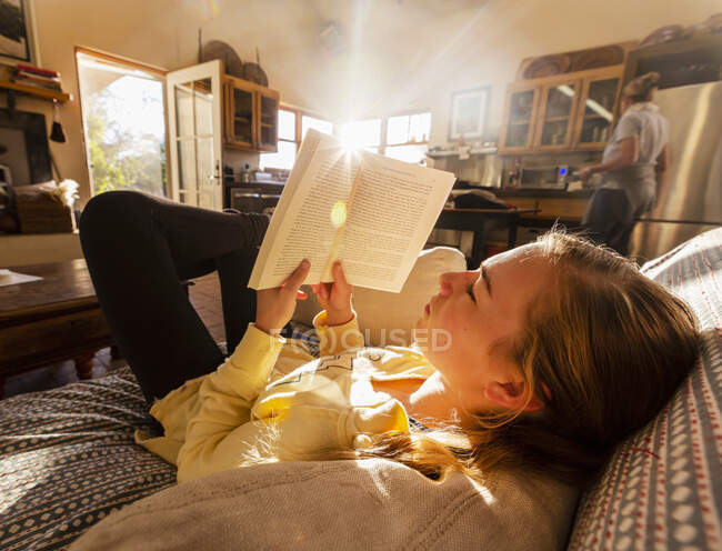 Adolescente leyendo libro en casa en la luz de la mañana temprano - foto de stock