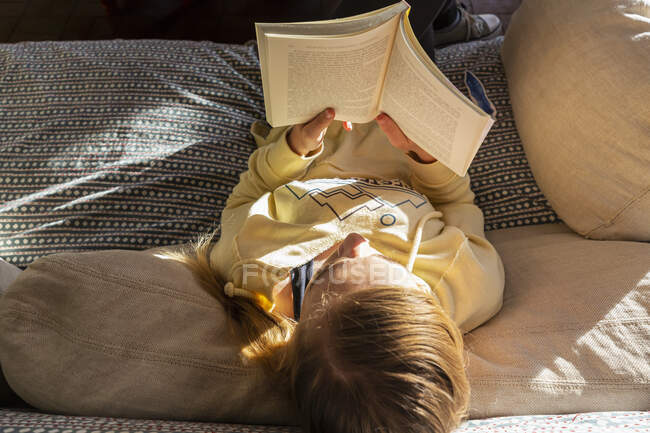 Дівчина-підліток читає книгу вдома в ранковому світлі — стокове фото
