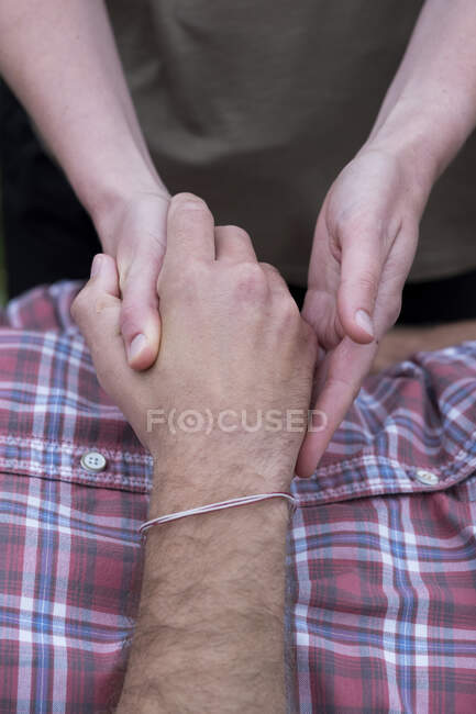 Hombre en un sofá, un terapeuta sosteniendo su mano, terapia de tacto curativo. - foto de stock