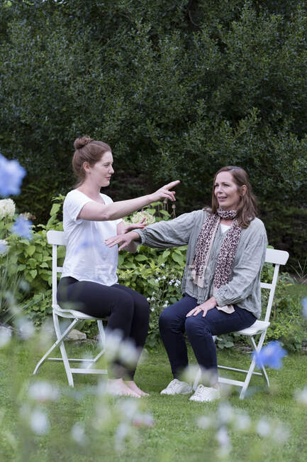Mujer y terapeuta sentadas en una sesión de terapia alternativa en un jardín. - foto de stock