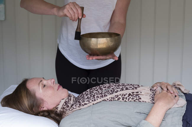 Mujer en un sofá, y una terapeuta usando un cuenco tibetano, terapia de sonido - foto de stock