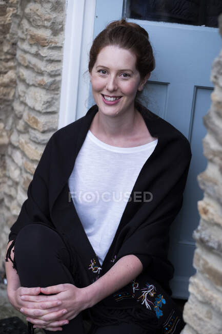Portrait de femme assise sur le pas de sa porte, souriant à la caméra. — Photo de stock