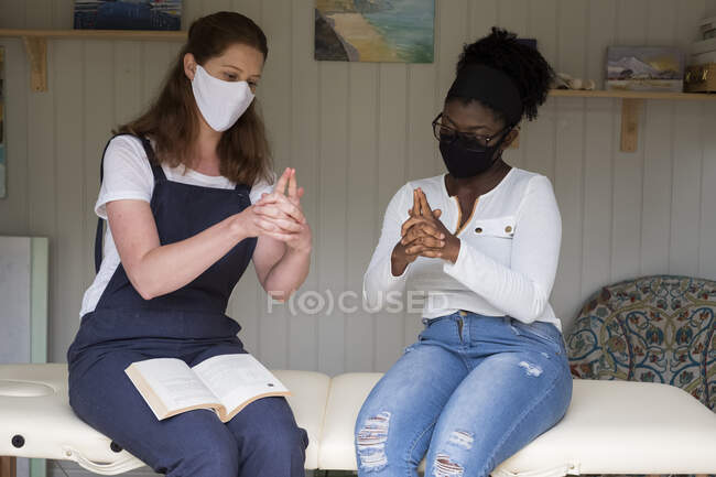 Woman and female therapist in face masks, hands steepled, EFT therapy — Stock Photo