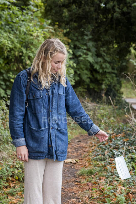 Young blond woman standing in forest, throwing away surgical face mask. — Stock Photo
