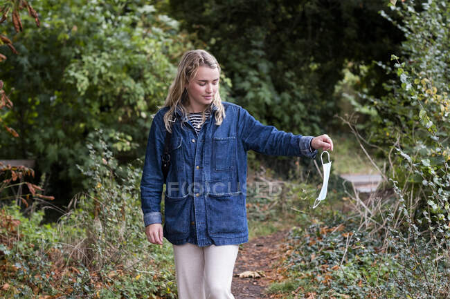 Junge blonde Frau steht im Wald und wirft OP-Mundschutz weg. — Stockfoto