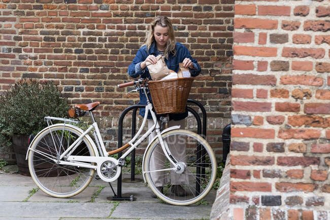 Жінка в масці для обличчя влаштовує паперові сумки для покупок у кошику для велосипедів — стокове фото