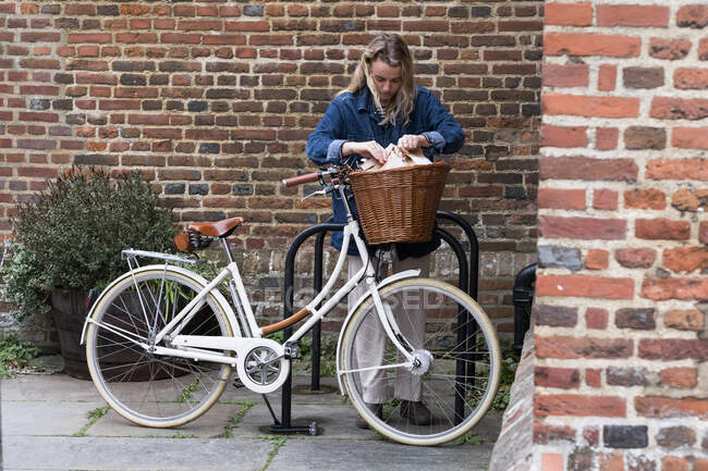 Жінка в масці для обличчя влаштовує паперові сумки для покупок у кошику для велосипедів — стокове фото