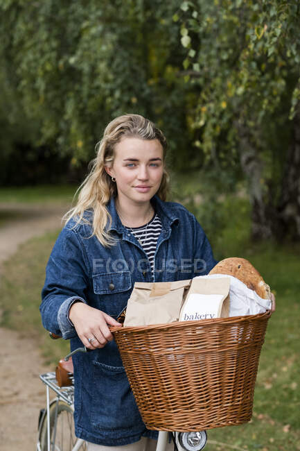 Young blond woman on bicycle with basket, smiling at camera. — Stock Photo