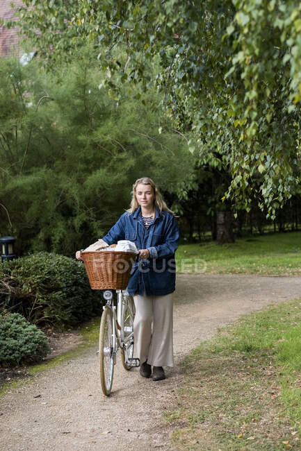 Giovane donna bionda spingendo in bicicletta con cesto lungo il sentiero. — Foto stock