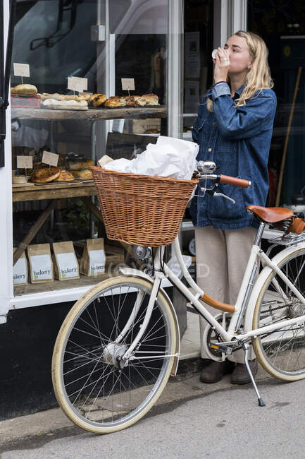 Молодая блондинка, стоящая рядом с велосипедом рядом с магазином пищевых продуктов. — стоковое фото